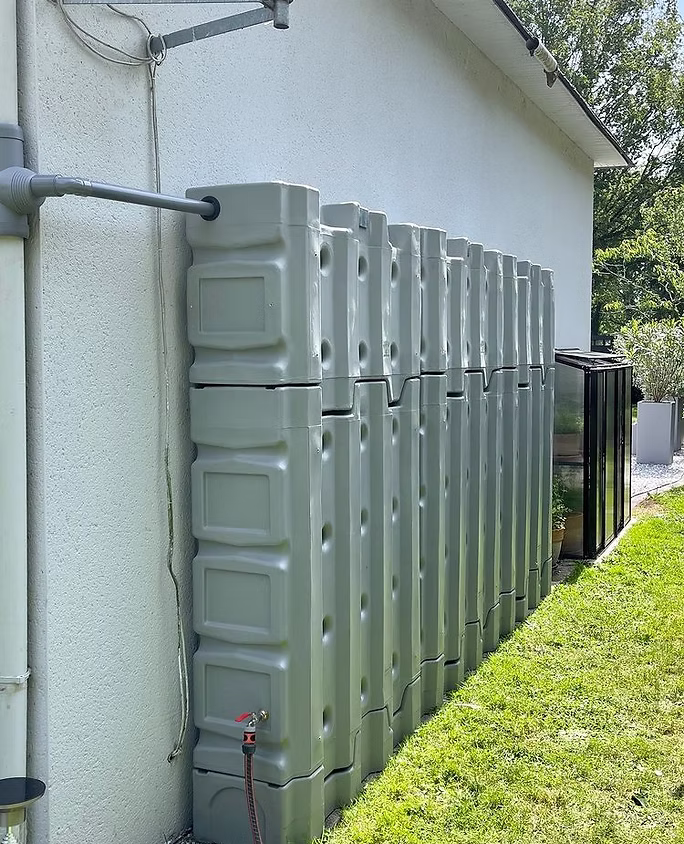 Récupérateur d'eau de pluie aérien Murdeau coloris gris pierre installé contre un mur